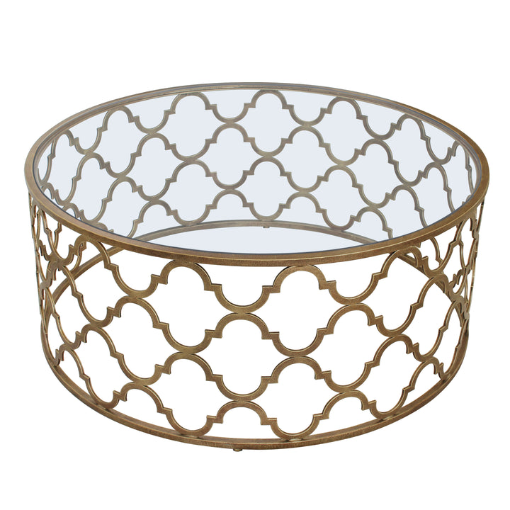 A coffee table with a geometric patterned base, painted in an antique gold finish topped with clear glass