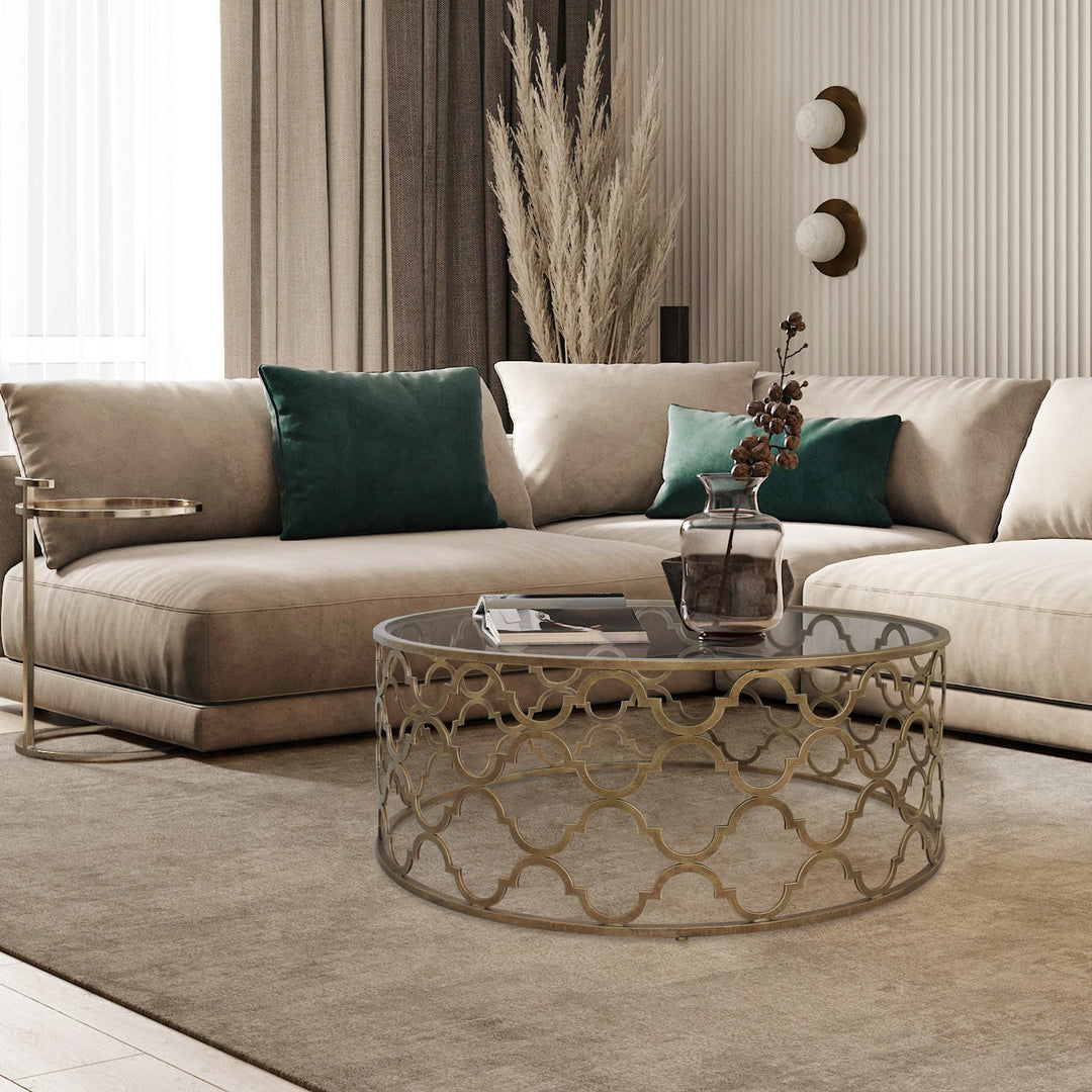 Round metal coffee table with quatrefoil pattern topped with glass in a contemporary living space