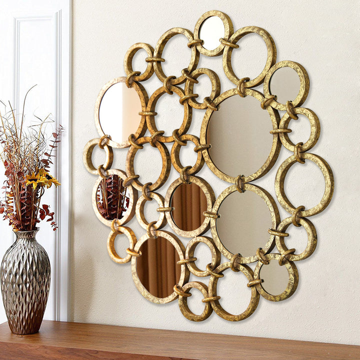 A modern mirror made of a combination of metal rings joined together and painted in an antique golden finish, hangs on a wall above a console table