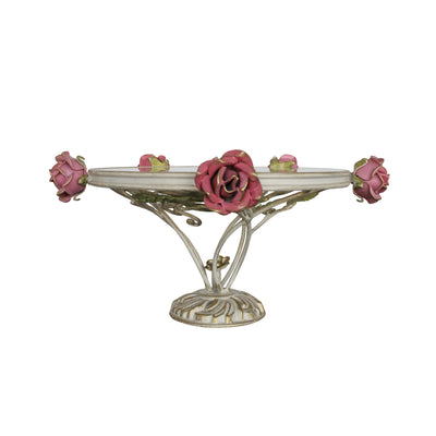 A decorative cake stand with a base adorned with leaves and roses inspired from nature topped with a round clear glass