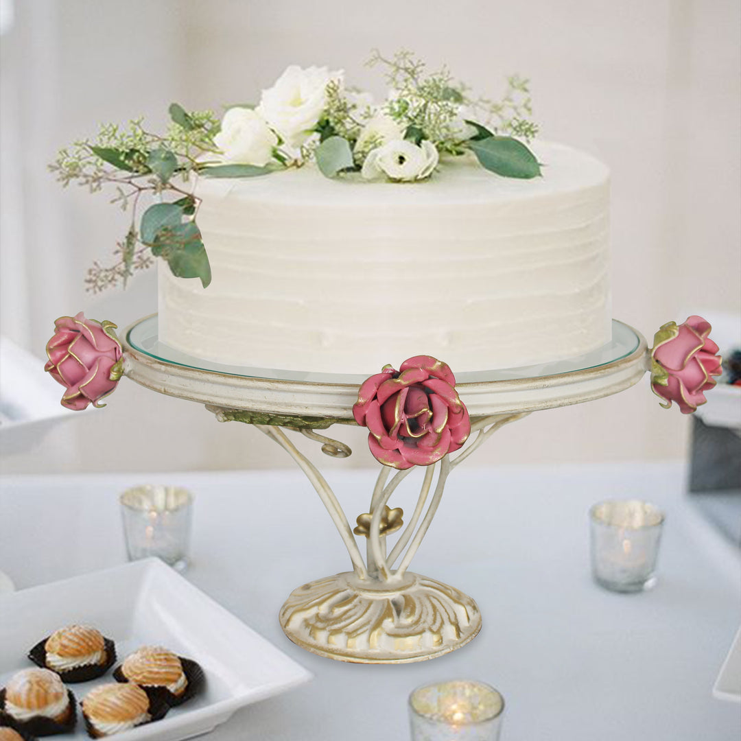 A cake sits on a decorative stand adorned with pink roses on a dining table