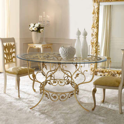 A classical round entry table with a wrought iron base and a clear glass top in a luxurious entrance hall