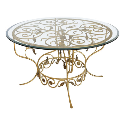 A luxurious round lobby table with a classical metal forged golden base, topped with a clear circular glass