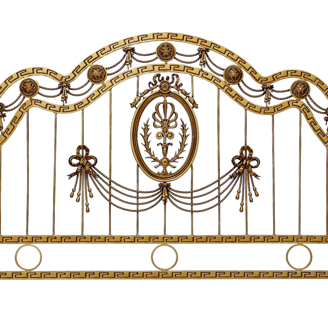 Close up of a wrought iron headboard made up of classical motifs and a versace pattern, painted in an antique golden finish