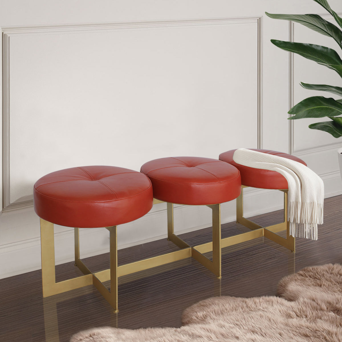 A modern metal golden bench topped with three round cushions upholstered in red leather