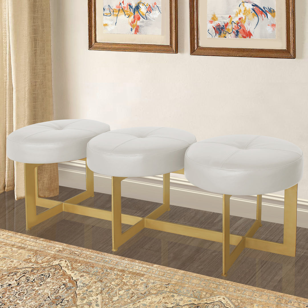 A modern metal golden bench topped with three round cushions upholstered in white leather