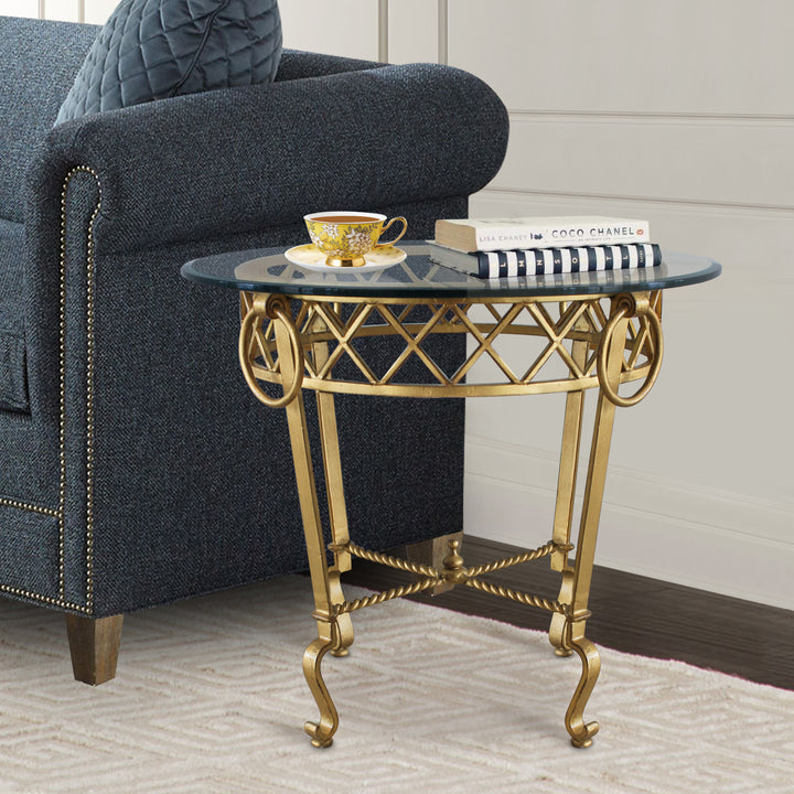 Classical style golden side table topped with clear glass stands beside a dark blue upholstered couch