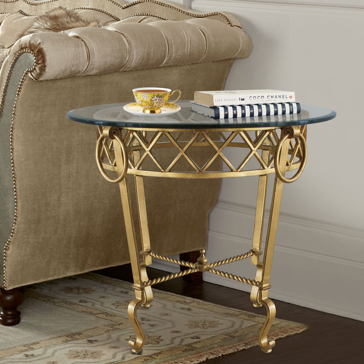 Classical style golden side table topped with clear glass stands beside a beige upholstered couch