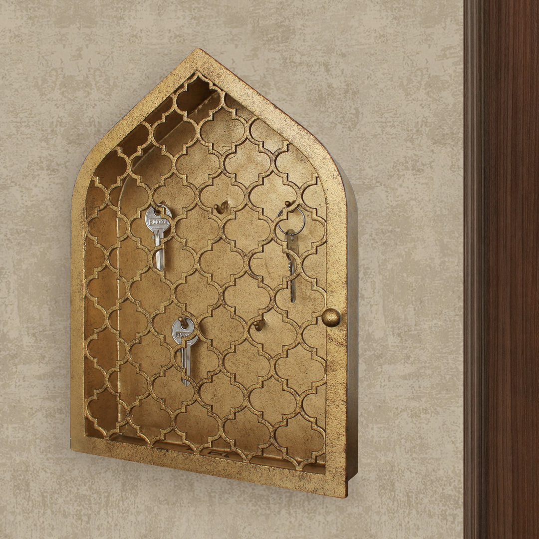 Key cabinet with a quatrefoil pattern and a pointed arched top painted in an antique gold finish wall mounted beside a wooden door